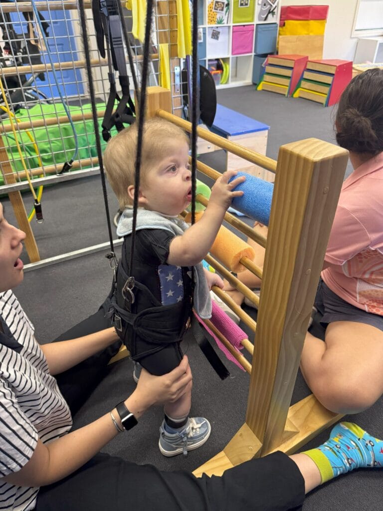 Child engaged in standing activity using a paediatric harness with therapist support