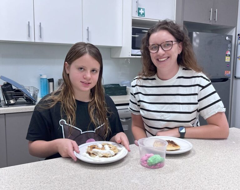 A girl and a smiling woman posing at a kitchen counter with plates of freshly prepared waffles.