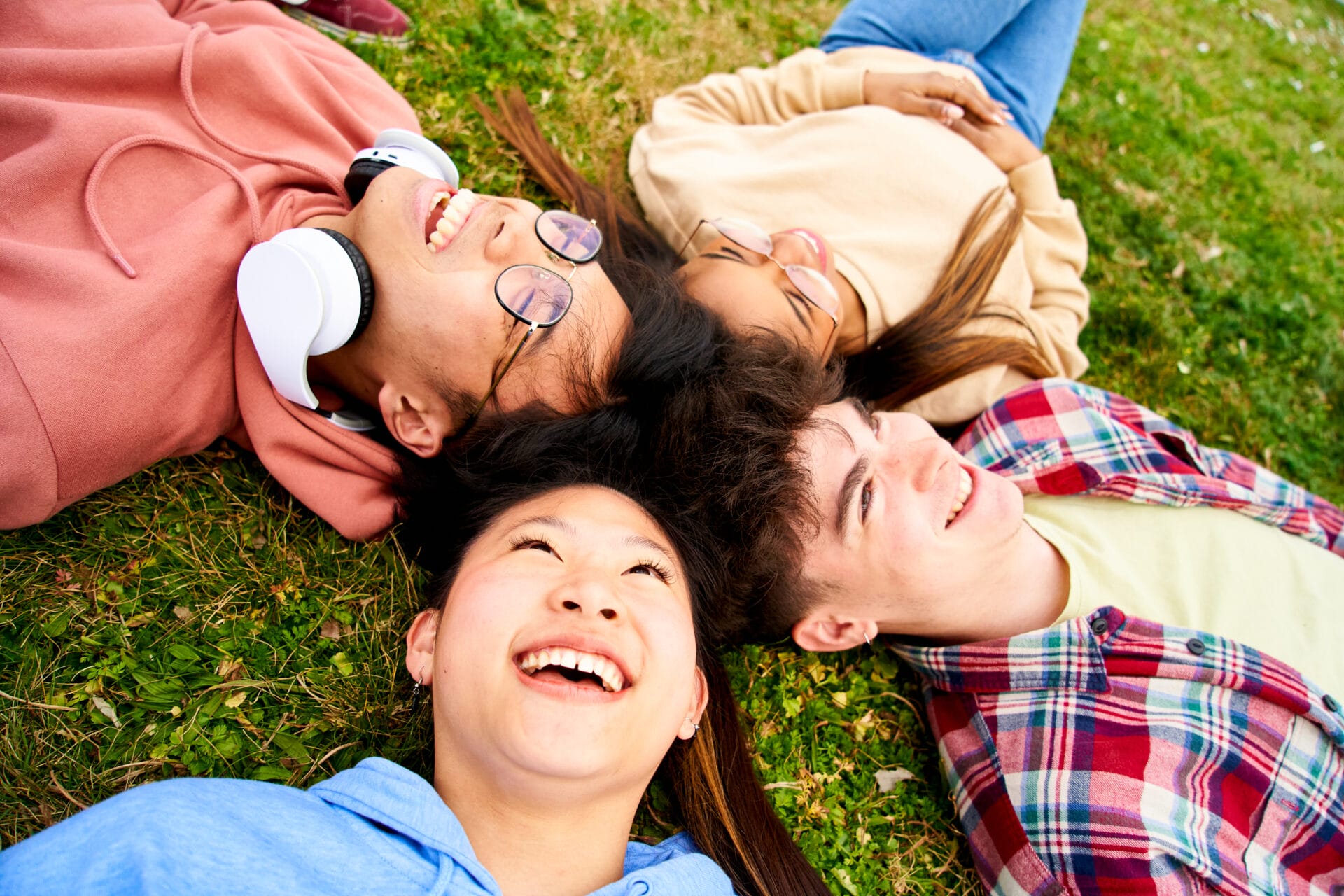 Close up shot of confident multiracial group of students smiling lying in a circle on the grass
