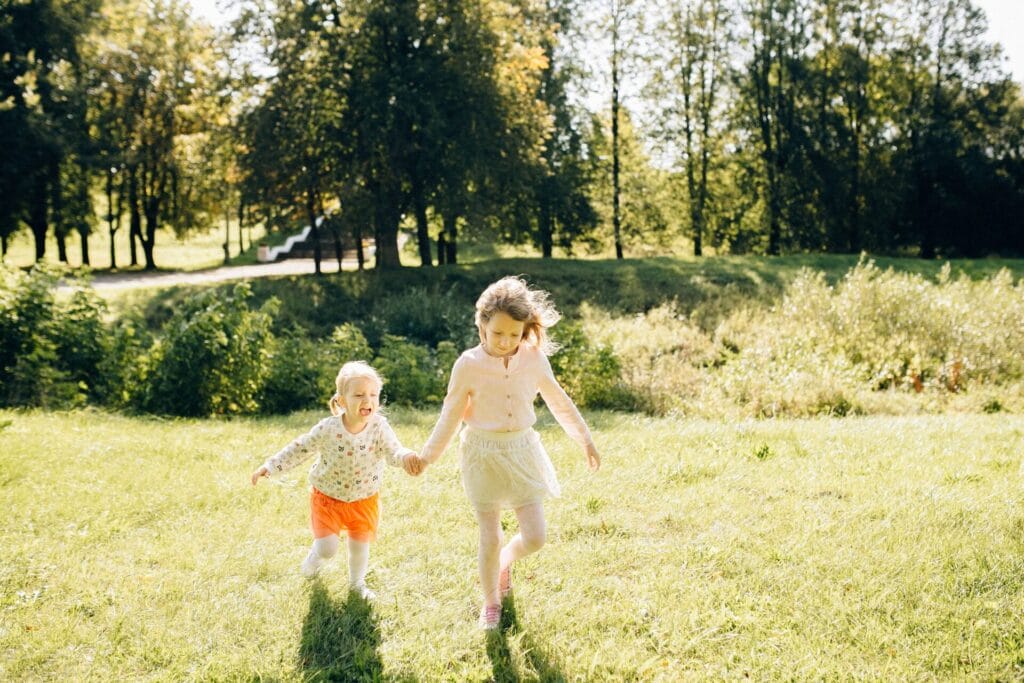 Two young children running together across sunlit grass, using balance and core stability as they move.