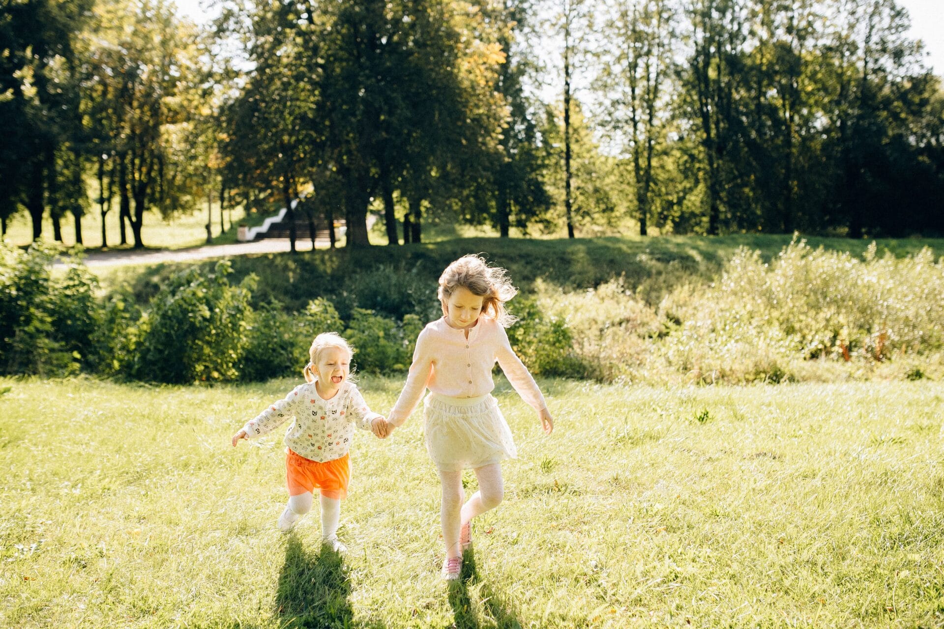 Two young children running together across sunlit grass, using balance and core stability as they move.